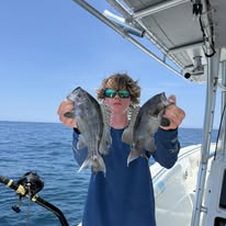 Person holding two fish on a boat in sunny weather.