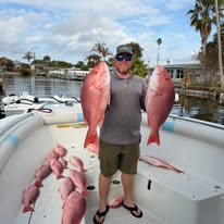 Person holding two large fish on a boat with more fish on the deck.