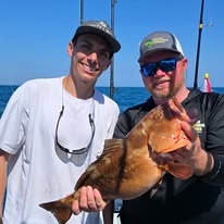 Two men on a boat holding a large fish, smiling at the camera.