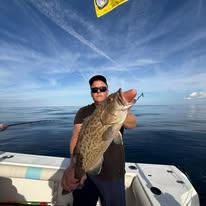 Person on boat holding large fish against clear sky.