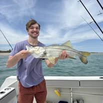Person smiling, holding a fish on a boat with a cloudy sky background.