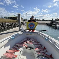 Person on boat dock holding a fishing flag with numerous fish laid out on the deck.