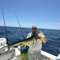 Person holding a large fish on a boat in the ocean under a clear blue sky.