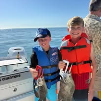 Two boys in life jackets holding fish on a boat.