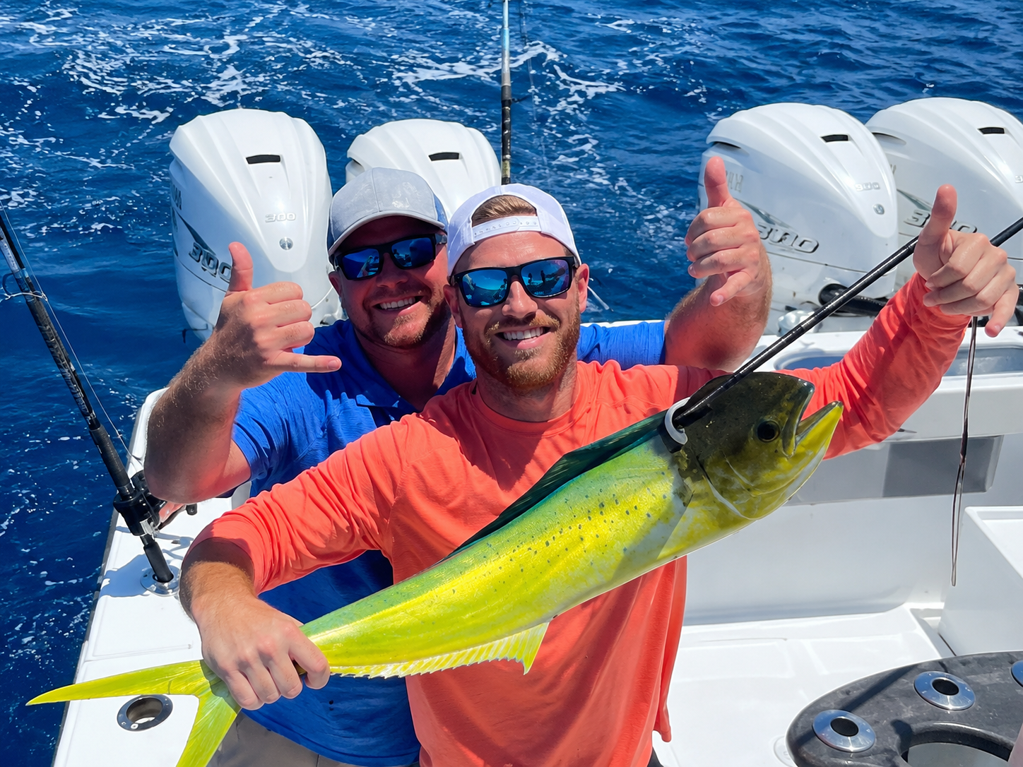 Two men on a boat holding a large yellow fish, both smiling and giving a thumbs-up.