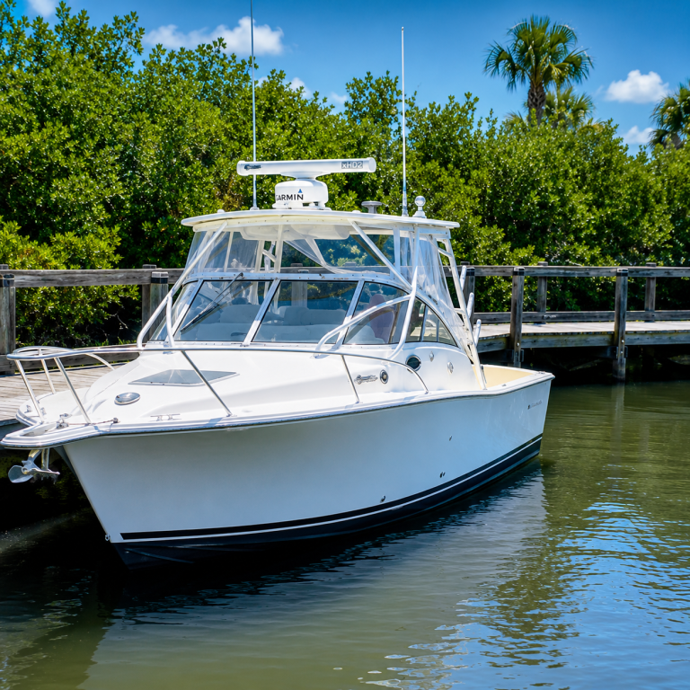 White boat moored by a wooden dock, surrounded by green foliage.
