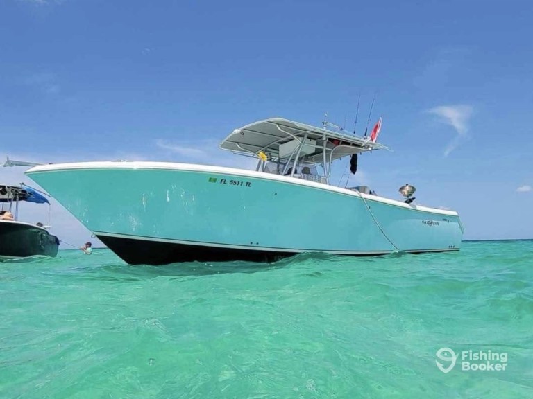 A turquoise fishing boat on clear water with a blue sky.