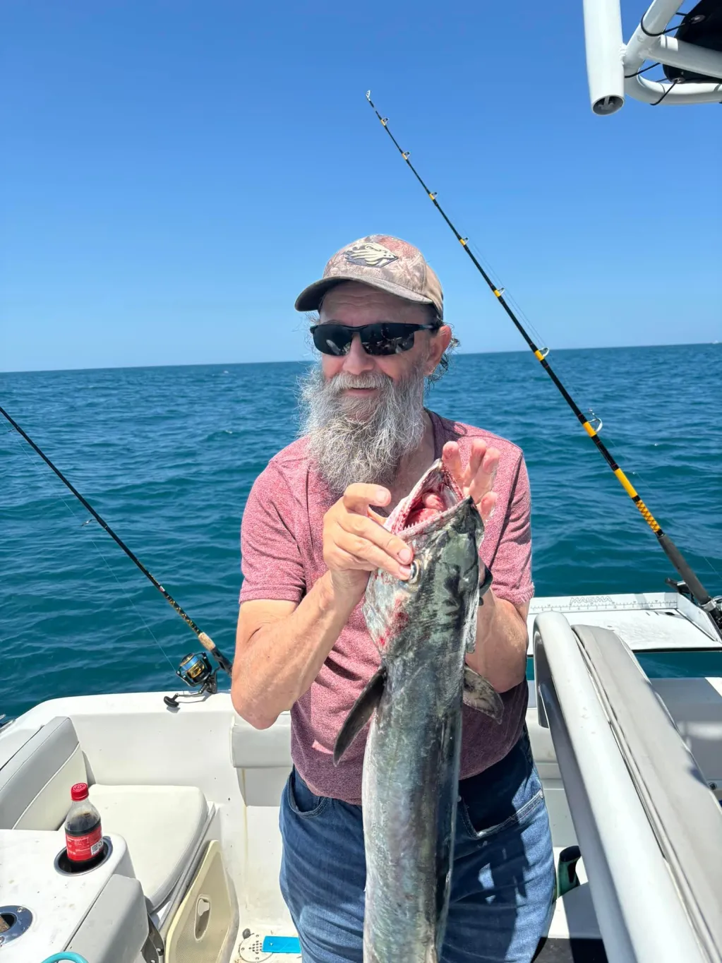 Man holding a fish on a boat with fishing rods and ocean background.